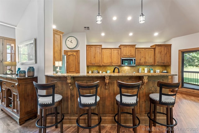 33268 Cardinal Dr, Afton, OK 74331 - kitchen featuring stainless steel microwave, decorative backsplash, light stone counters, lofted ceiling, and brown cabinets