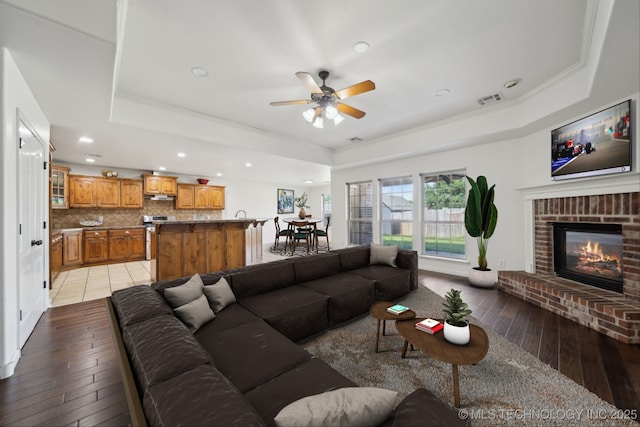12523 S Cedar Pl, Jenks, OK 74037 - living area with a raised ceiling, light wood-style flooring, ceiling fan, recessed lighting, and a fireplace