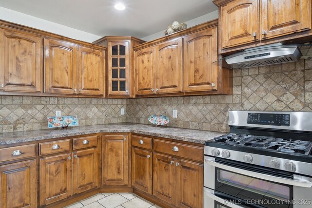 12523 S Cedar Pl, Jenks, OK 74037 - kitchen featuring gas range, brown cabinets, glass insert cabinets, light tile patterned flooring, and under cabinet range hood