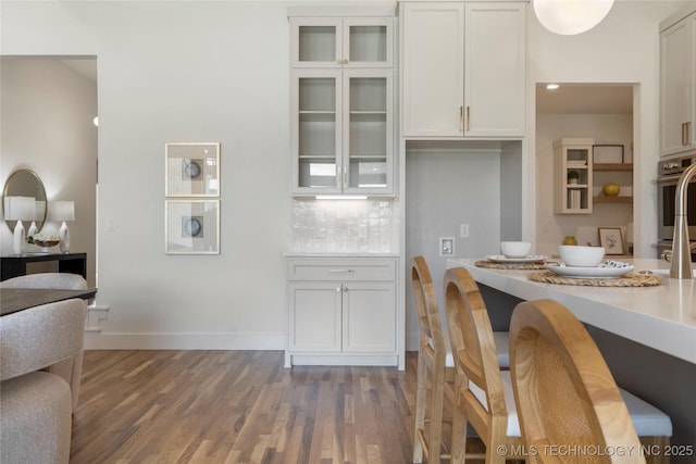 2338 E 134th St S, Bixby, OK 74008 - kitchen featuring wood finished floors, white cabinetry, light countertops, glass insert cabinets, and tasteful backsplash