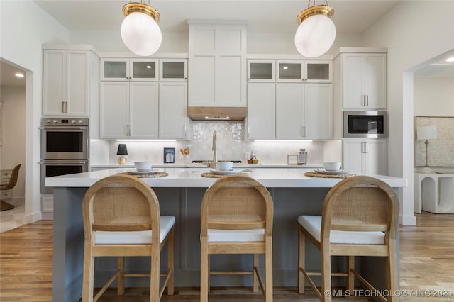 2338 E 134th St S, Bixby, OK 74008 - kitchen featuring stainless steel appliances, a center island with sink, tasteful backsplash, light countertops, and hanging light fixtures