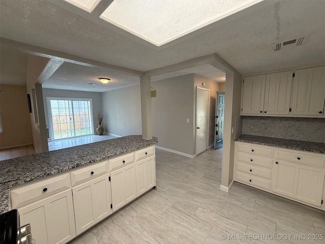 2800 E Seattle St, Broken Arrow, OK 74014 - kitchen with dark stone counters, a textured ceiling, light marble finish flooring, white cabinetry, and baseboards