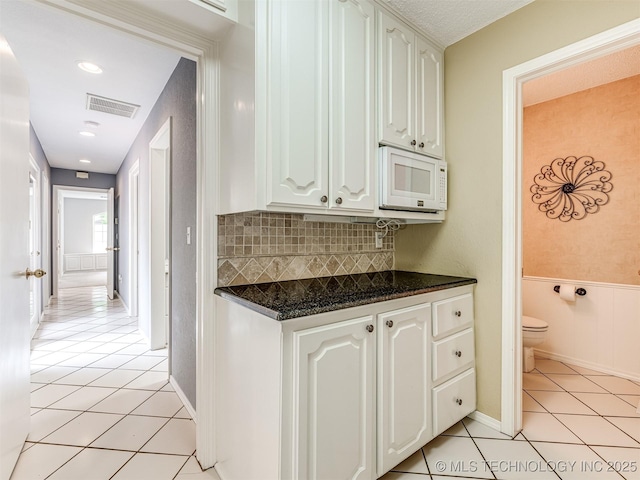 406 Sequoyah Trl, Norman, OK 73071 - kitchen featuring light tile patterned floors, white microwave, white cabinetry, decorative backsplash, and a wainscoted wall