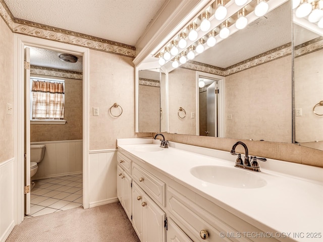 406 Sequoyah Trl, Norman, OK 73071 - full bath with a textured ceiling, toilet, double vanity, wainscoting, and wallpapered walls