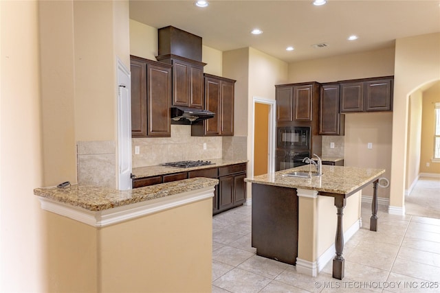 1425 Switchgrass, Edmond, OK 73013 - kitchen with black appliances, under cabinet range hood, light stone counters, a sink, and arched walkways