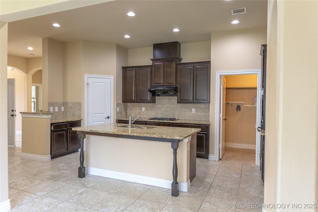 1425 Switchgrass, Edmond, OK 73013 - kitchen featuring under cabinet range hood, a sink, arched walkways, decorative backsplash, and a center island with sink