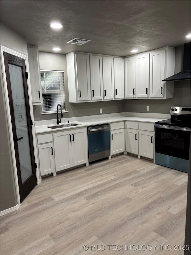 413 E 8th St, Cushing, OK 74023 - kitchen featuring stainless steel appliances, a sink, wall chimney exhaust hood, light countertops, and light wood-style floors