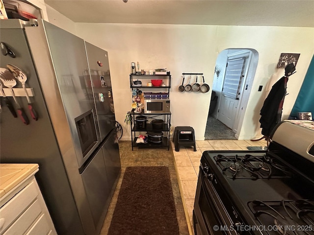 661 12th NW, Ardmore, OK 73401 - kitchen with gas range, stainless steel fridge with ice dispenser, and light tile patterned flooring