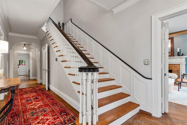 319 E 21st St, Tulsa, OK 74114 - stairway with wood finished floors, crown molding, arched walkways, baseboards, and a fireplace