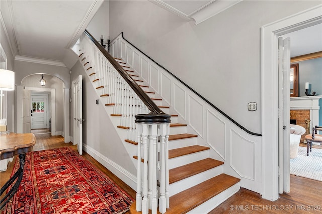 319 E 21st St, Tulsa, OK 74114 - stairway featuring crown molding, wood finished floors, arched walkways, and a brick fireplace
