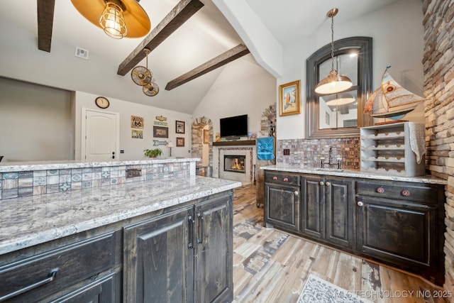 30907 E 68th St S, Broken Arrow, OK 74014 - kitchen with beam ceiling, a glass covered fireplace, light wood-type flooring, light stone countertops, and backsplash