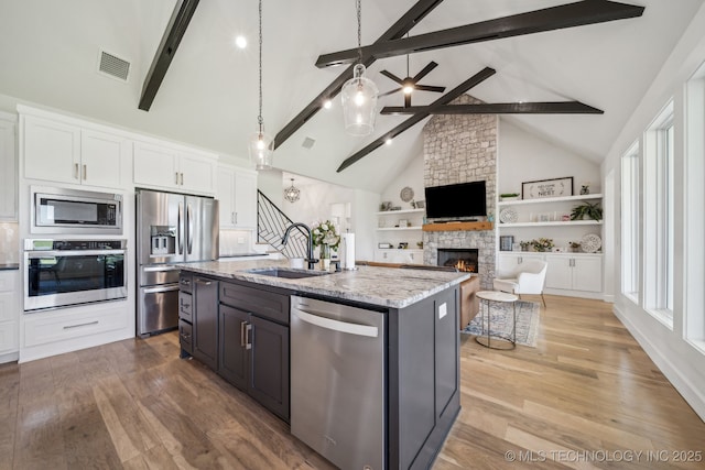 123 S 168th St, Glenpool, OK 74033 - kitchen with stainless steel appliances, a fireplace, light stone countertops, beam ceiling, and an island with sink