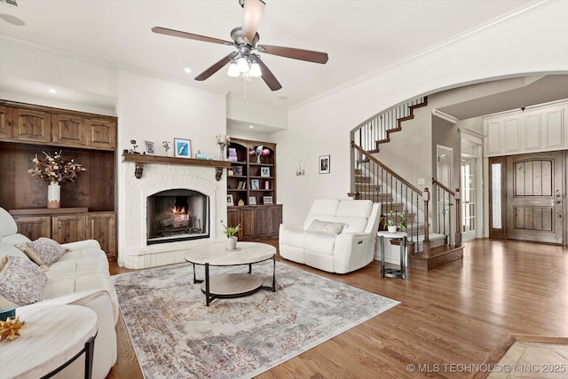 12643 S 67th E Ave, Bixby, OK 74070 - living room featuring stairway, crown molding, a ceiling fan, light wood-style flooring, and a warm lit fireplace