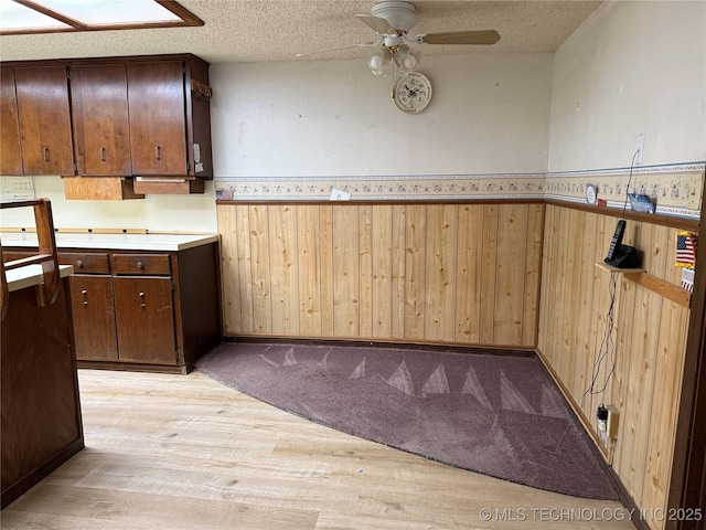 2099 S 80th St E, Muskogee, OK 74403 - kitchen featuring light wood-style floors, wainscoting, a ceiling fan, wood walls, and light countertops