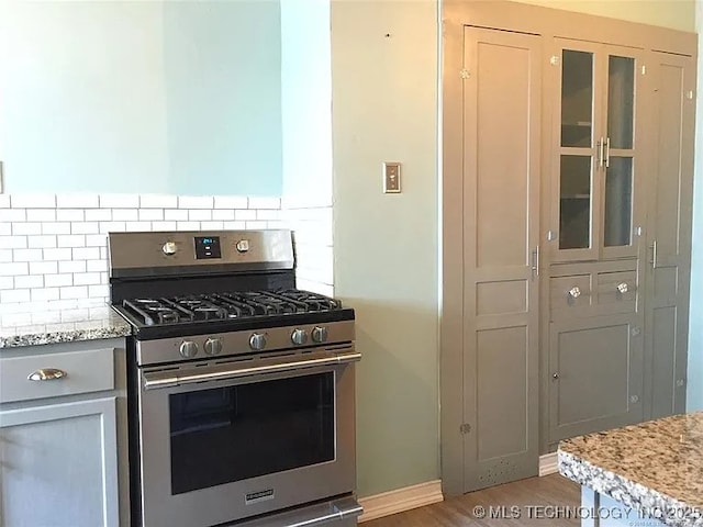 403 W Broadway, Marietta, OK 73448 - kitchen featuring stainless steel range with gas stovetop, backsplash, wood finished floors, glass insert cabinets, and light stone countertops