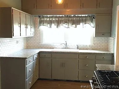 403 W Broadway, Marietta, OK 73448 - kitchen featuring decorative backsplash, light countertops, gray cabinets, and a sink