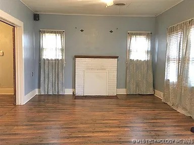 403 W Broadway, Marietta, OK 73448 - unfurnished living room with wood finished floors, plenty of natural light, a fireplace, and crown molding