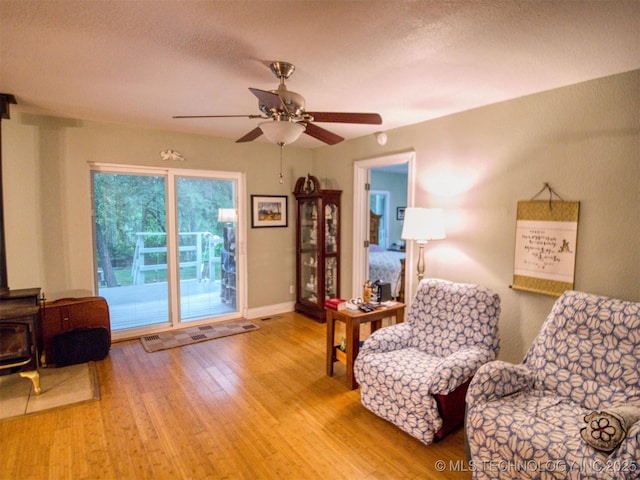 5404 Ranch Rd, Kingston, OK 73439 - sitting room with a wood stove, wood finished floors, a ceiling fan, and baseboards