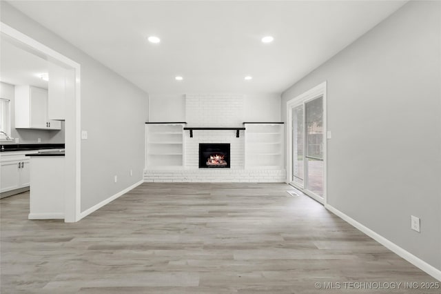 11607 E 24th St, Tulsa, OK 74129 - unfurnished living room featuring recessed lighting, light wood-type flooring, baseboards, a brick fireplace, and a sink