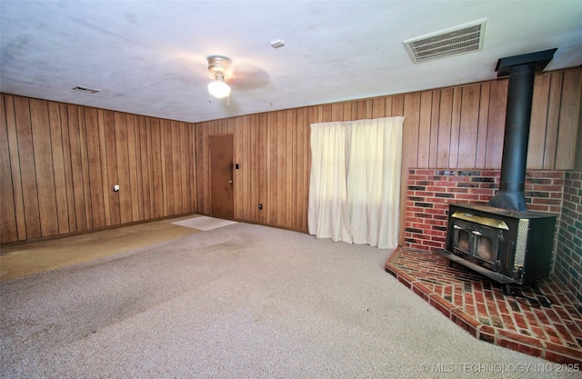 4120 W 53rd St S, Muskogee, OK 74401 - unfurnished living room featuring a wood stove, carpet flooring, wooden walls, and ceiling fan