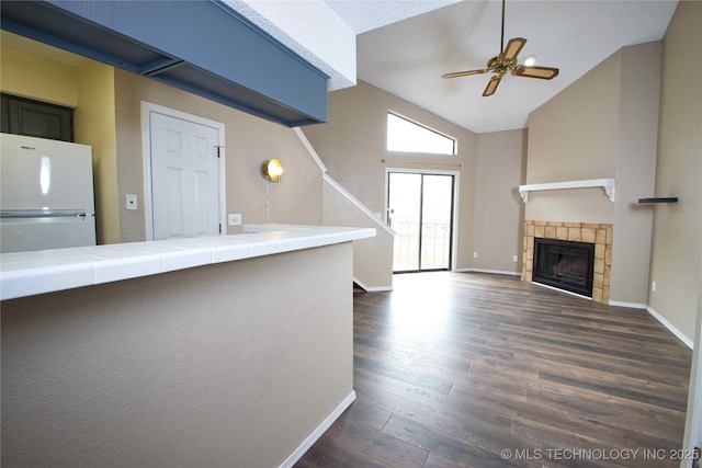 6737 S Peoria Ave Unit C213, Tulsa, OK 74136 - unfurnished living room with dark wood-type flooring, a ceiling fan, vaulted ceiling, baseboards, and a tile fireplace