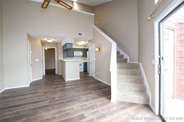 6737 S Peoria Ave Unit C213, Tulsa, OK 74136 - unfurnished living room featuring a ceiling fan, dark wood finished floors, stairway, a towering ceiling, and baseboards