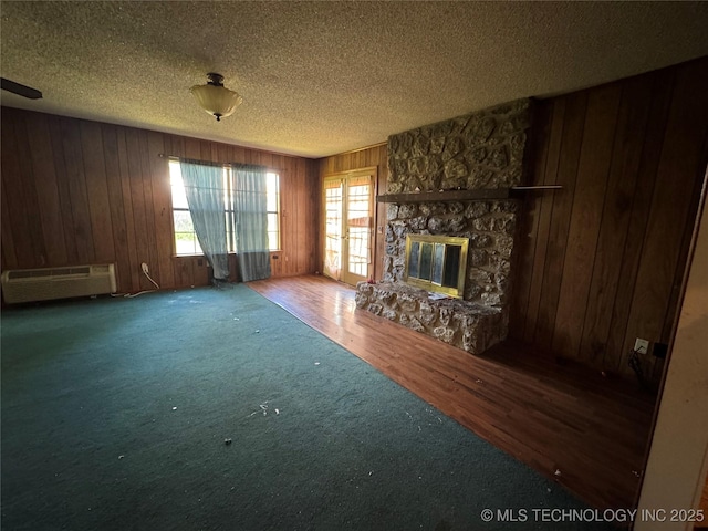 10653 E 18th St, Tulsa, OK 74128 - unfurnished living room with wooden walls, a stone fireplace, carpet flooring, a textured ceiling, and a wall mounted AC