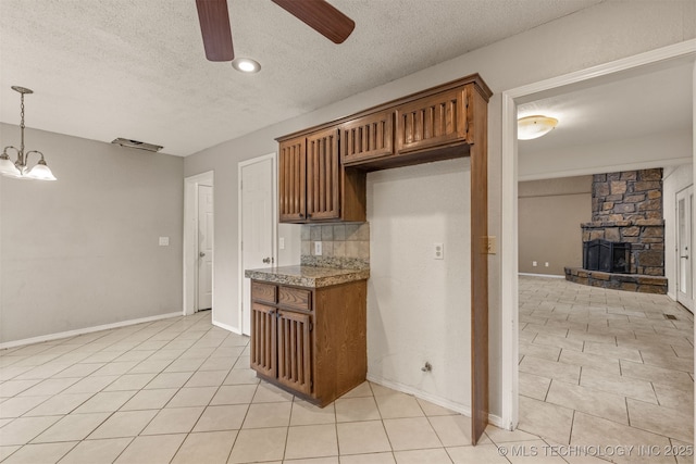 8424 Harp Blvd, Broken Arrow, OK 74014 - kitchen featuring ceiling fan, a textured ceiling, light tile patterned floors, a stone fireplace, and brown cabinets