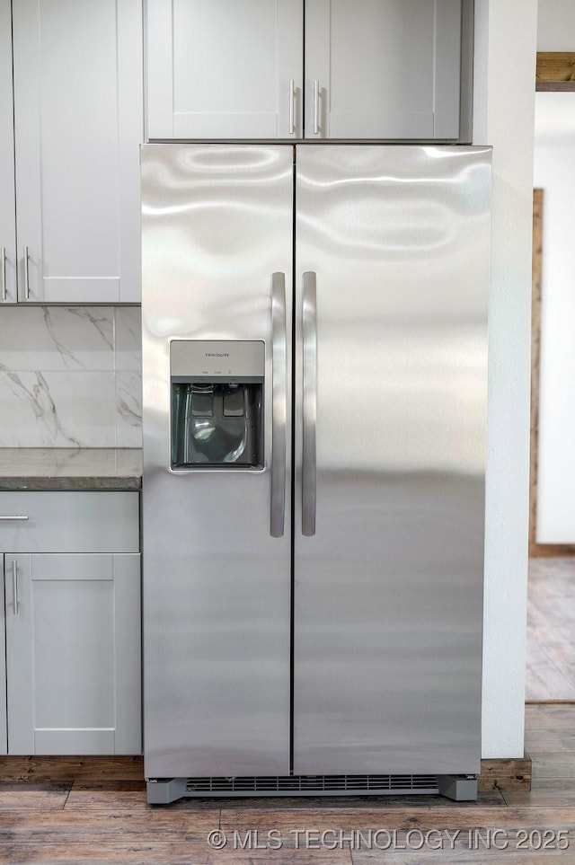 984 Ridgepoint, Fort Towson, OK 74735 - detailed view of stainless steel fridge with ice dispenser, white cabinetry, light stone countertops, and wood finished floors