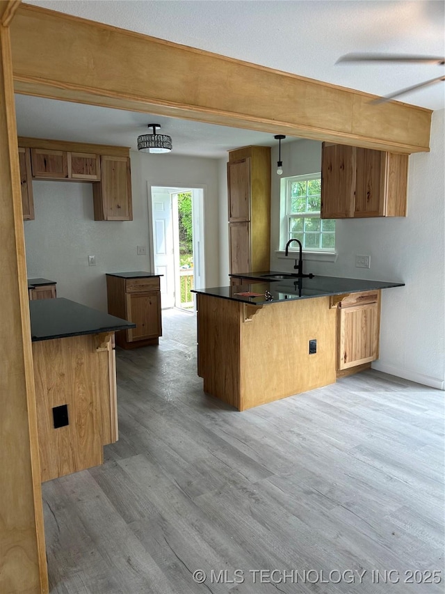 4613 N Main St E, Tulsa, OK 74115 - kitchen featuring dark countertops, a peninsula, light wood-type flooring, a sink, and brown cabinetry