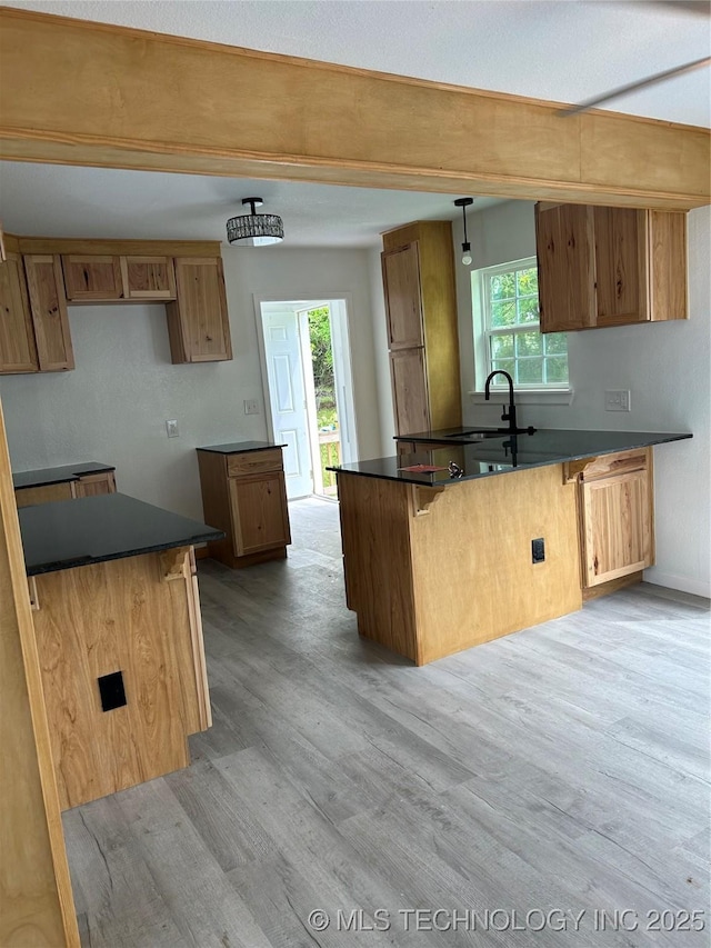 4613 N Main St E, Tulsa, OK 74115 - kitchen featuring dark countertops, light wood-type flooring, beam ceiling, a peninsula, and brown cabinets