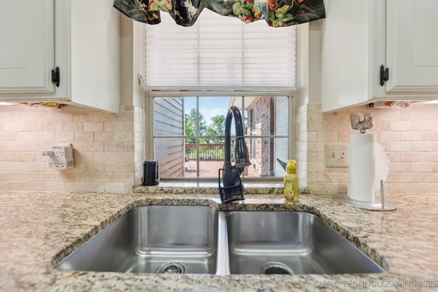 805 E 10th St, Claremore, OK 74017 - kitchen view of a sink, backsplash, white cabinetry, and light stone counters