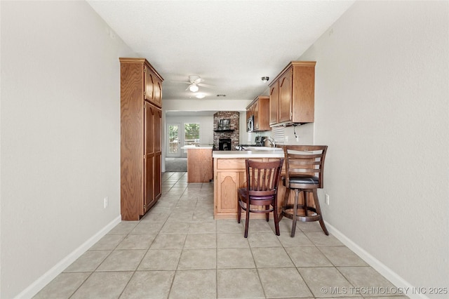 1309 N Willow Ave, Broken Arrow, OK 74012 - kitchen with a peninsula, ceiling fan, light tile patterned flooring, light countertops, and brown cabinetry