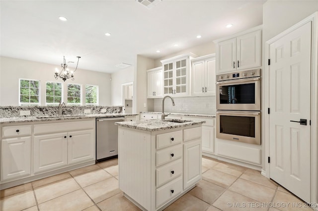 13041 E 67th St, Broken Arrow, OK 74012 - kitchen with stainless steel appliances, a sink, decorative backsplash, a center island with sink, and a chandelier