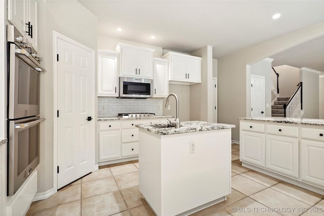 13041 E 67th St, Broken Arrow, OK 74012 - kitchen with stainless steel appliances, a sink, decorative backsplash, a center island with sink, and light tile patterned flooring