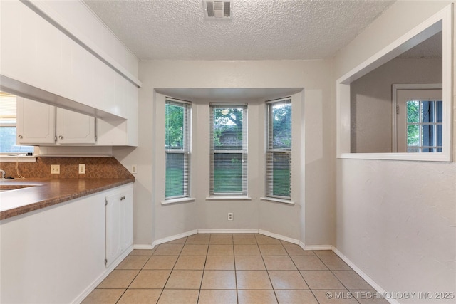 901 S Lions Ave, Broken Arrow, OK 74012 - kitchen with plenty of natural light, white cabinets, a textured ceiling, light tile patterned flooring, and dark countertops