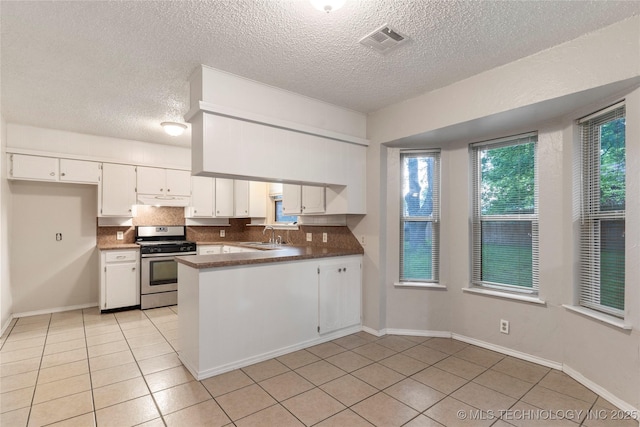 901 S Lions Ave, Broken Arrow, OK 74012 - kitchen with stainless steel gas stove, a textured ceiling, a peninsula, light tile patterned floors, and backsplash
