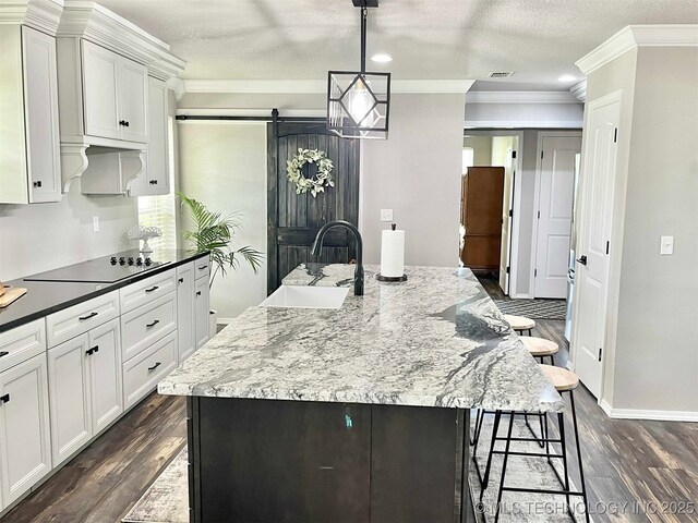 175 Johnson Rd, Broken Bow, OK 74728 - kitchen featuring black electric stovetop, a sink, crown molding, white cabinetry, and a breakfast bar