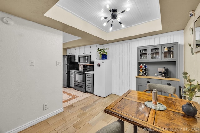 6356 S 80th E Ave Unit 25C, Tulsa, OK 74133 - dining room featuring a chandelier, a raised ceiling, light wood-style floors, and baseboards