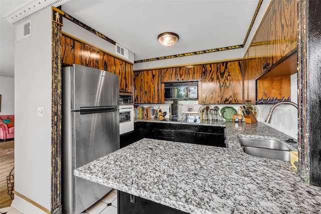 611 W 15th St Unit F1, Tulsa, OK 74127 - kitchen featuring freestanding refrigerator, a sink, a peninsula, light stone countertops, and brown cabinets