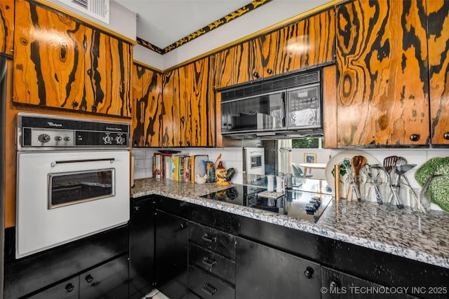 611 W 15th St Unit F1, Tulsa, OK 74127 - kitchen featuring black appliances, decorative backsplash, light stone countertops, and brown cabinets