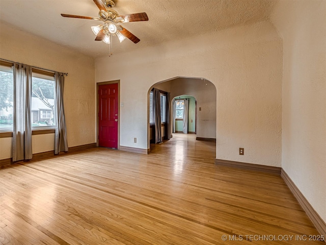 3504 E Haskell St, Tulsa, OK 74115 - unfurnished room featuring arched walkways, ceiling fan, light wood-type flooring, plenty of natural light, and a textured wall