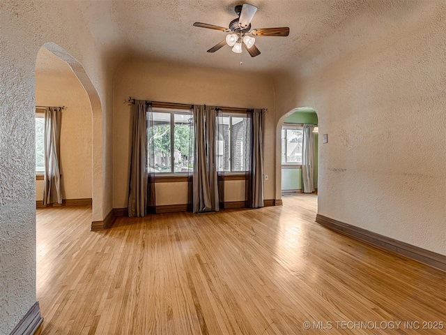 3504 E Haskell St, Tulsa, OK 74115 - empty room featuring arched walkways, a textured wall, light wood finished floors, a ceiling fan, and a textured ceiling