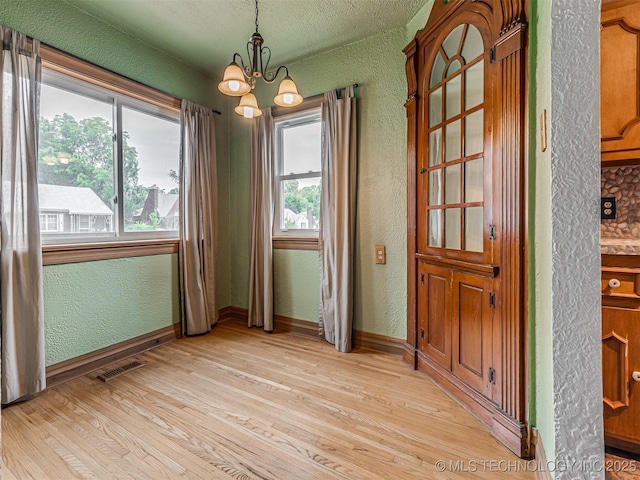 3504 E Haskell St, Tulsa, OK 74115 - unfurnished dining area featuring a textured wall, a chandelier, light wood-style flooring, a textured ceiling, and baseboards