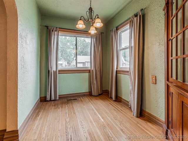 3504 E Haskell St, Tulsa, OK 74115 - unfurnished dining area featuring a textured wall, light wood-type flooring, a chandelier, arched walkways, and baseboards