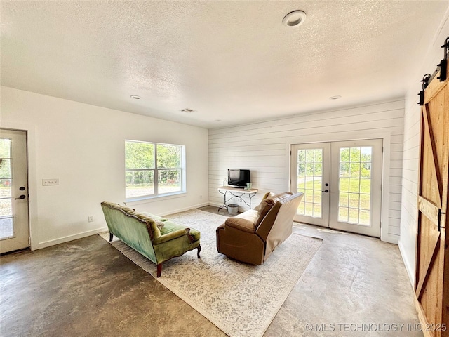 157 Canna Ln, Mcalester, OK 74501 - living area featuring unfinished concrete flooring, a barn door, a textured ceiling, wooden walls, and french doors