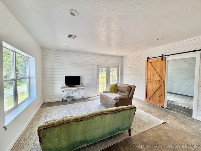 157 Canna Ln, Mcalester, OK 74501 - living room featuring healthy amount of natural light, french doors, a barn door, wood walls, and concrete floors