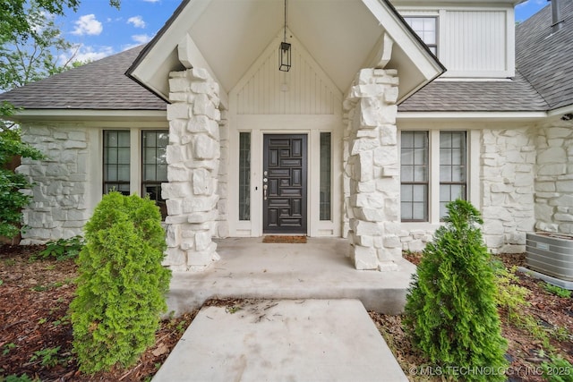 11033 E 66th St, Tulsa, OK 74133 - doorway to property featuring stone siding, a shingled roof, and central AC unit