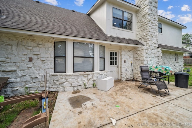 11033 E 66th St, Tulsa, OK 74133 - rear view of house featuring stone siding, a shingled roof, a patio, and a chimney