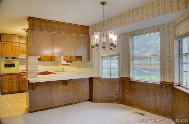 4004 S Hickory Ave, Broken Arrow, OK 74011 - kitchen featuring oven, wallpapered walls, a chandelier, brown cabinetry, and healthy amount of natural light